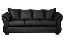 Full indoor shot of a black three-seat sofa. The sofa is a dark, solid black color. It features gently curved armrests and a slightly raised back, characteristic of a contemporary style. The cushions appear to be filled and are upholstered in the same material as the rest of the sofa. The sofa's lines are smooth and the overall impression is of a comfortable and modern piece of furniture. The sofa sits on four, visible, slightly angled, dark brown/black legs. The background is pure white, isolating the sofa as the central focus.