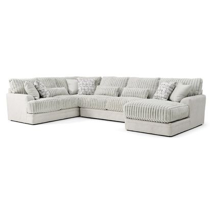 A modern, U-shaped sectional sofa in a light gray fabric with a ribbed texture is displayed against a plain white background. The sofa features a chaise lounge on the right side and plush, cushioned seating with a deep, comfortable design. It is adorned with several decorative pillows, including rectangular and square shapes, some with subtle white and gray patterned designs. The overall style is contemporary and cozy, suitable for a living room setting.