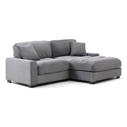 The Arizona Loveseat Chaise is a modern, L-shaped sectional sofa with a sleek, contemporary, and minimalist design. The sofa is upholstered in a soft, grey fabric with a subtle, vertical striped texture that adds a touch of visual interest. The sectional has a right-facing chaise lounge, extending from the main seating area, which provides a comfortable spot for lounging or reclining. The sofa's structure includes thick, cushioned armrests on both ends, offering a cozy and supportive feel. The backrest is composed of large, tufted cushions that align with the seat cushions below, creating a uniform and plush appearance. The seat cushions are deep and tufted as well, suggesting a comfortable seating experience. Additionally, the sofa comes with two matching throw pillows, also in the same grey, striped fabric, placed on the backrest for extra comfort and aesthetic appeal. The sofa sits on small, square, black feet that provide a slight elevation from the floor, giving it a clean and grounded look. 