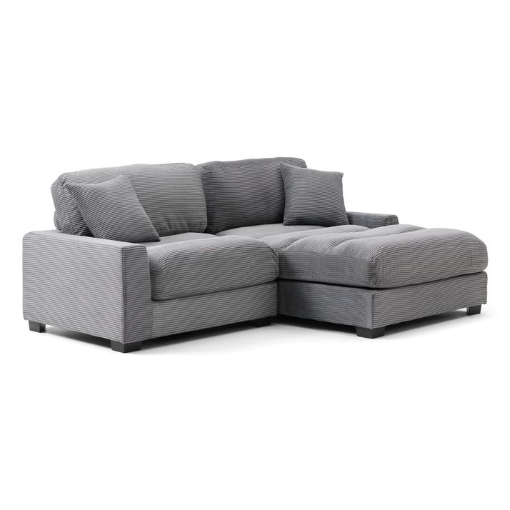 The Arizona Loveseat Chaise is a modern, L-shaped sectional sofa with a sleek, contemporary, and minimalist design. The sofa is upholstered in a soft, grey fabric with a subtle, vertical striped texture that adds a touch of visual interest. The sectional has a right-facing chaise lounge, extending from the main seating area, which provides a comfortable spot for lounging or reclining. The sofa's structure includes thick, cushioned armrests on both ends, offering a cozy and supportive feel. The backrest is composed of large, tufted cushions that align with the seat cushions below, creating a uniform and plush appearance. The seat cushions are deep and tufted as well, suggesting a comfortable seating experience. Additionally, the sofa comes with two matching throw pillows, also in the same grey, striped fabric, placed on the backrest for extra comfort and aesthetic appeal. The sofa sits on small, square, black feet that provide a slight elevation from the floor, giving it a clean and grounded look. 