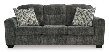 A three-seat sofa is presented in a gray-charcoal fabric with a textured, slightly mottled appearance.  The upholstery has a subtle pattern giving a variation in the shade throughout.  Three matching accent pillows, featuring a pattern of vertical stripes and light beige/cream tones against a darker gray background, are placed on the seat cushions. The sofa has gently curved armrests and dark-colored, faux-wood finish legs. The sofa is presented against a plain white background, which helps to highlight the sofa's color and texture.