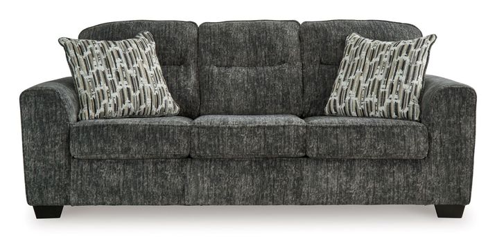 A three-seat sofa is presented in a gray-charcoal fabric with a textured, slightly mottled appearance.  The upholstery has a subtle pattern giving a variation in the shade throughout.  Three matching accent pillows, featuring a pattern of vertical stripes and light beige/cream tones against a darker gray background, are placed on the seat cushions. The sofa has gently curved armrests and dark-colored, faux-wood finish legs. The sofa is presented against a plain white background, which helps to highlight the sofa's color and texture.