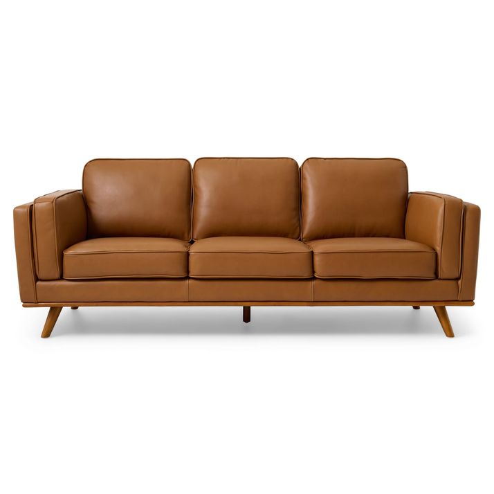A modern three-seater sofa with a sleek, minimalist design. The sofa is upholstered in a rich tan leather, giving it a luxurious and warm appearance. It features a clean-lined structure with three cushioned seats and matching backrests, each with a slightly tufted surface for added texture and comfort. The armrests are thick and padded, extending vertically to align with the backrests, contributing to a cohesive and sturdy look. The base of the sofa is supported by four angled wooden legs in a natural finish, adding a mid-century modern touch to the overall aesthetic. The background is a plain white, which highlights the sofa's design and color.